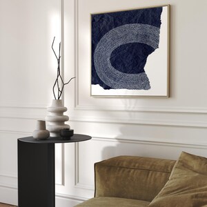 May include: A square canvas print with a white abstract design on a dark blue background. The design is a circle with a white outline and white dots inside. The canvas is textured and has a distressed look.
