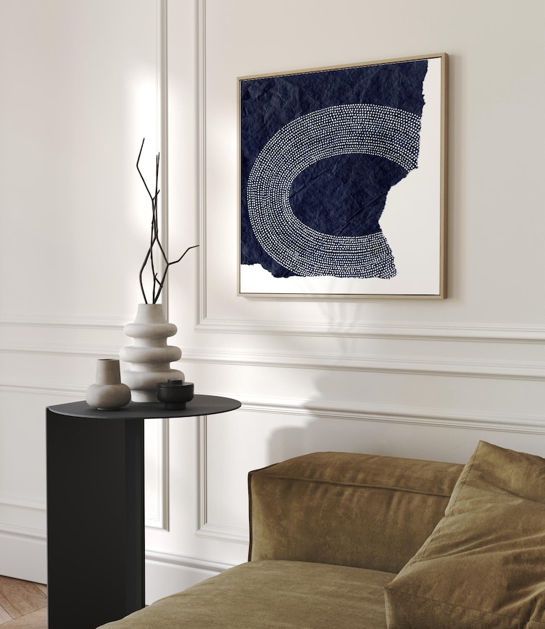 May include: A square canvas print with a white abstract design on a dark blue background. The design is a circle with a white outline and white dots inside. The canvas is textured and has a distressed look.