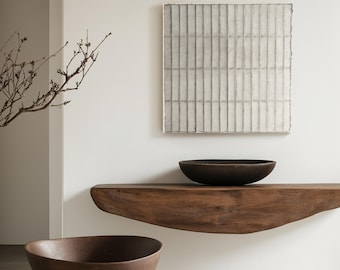 Puede incluir: Dos cuencos de madera marrón, uno en un estante de madera y otro en el suelo, en un interior minimalista con una pared blanca y una pintura abstracta cuadrada.