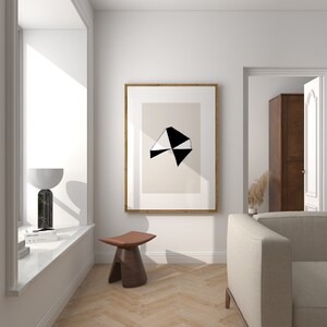 May include: A white and black geometric abstract art print in a wooden frame hangs on a white wall above a brown wooden stool. A white couch is in the background.