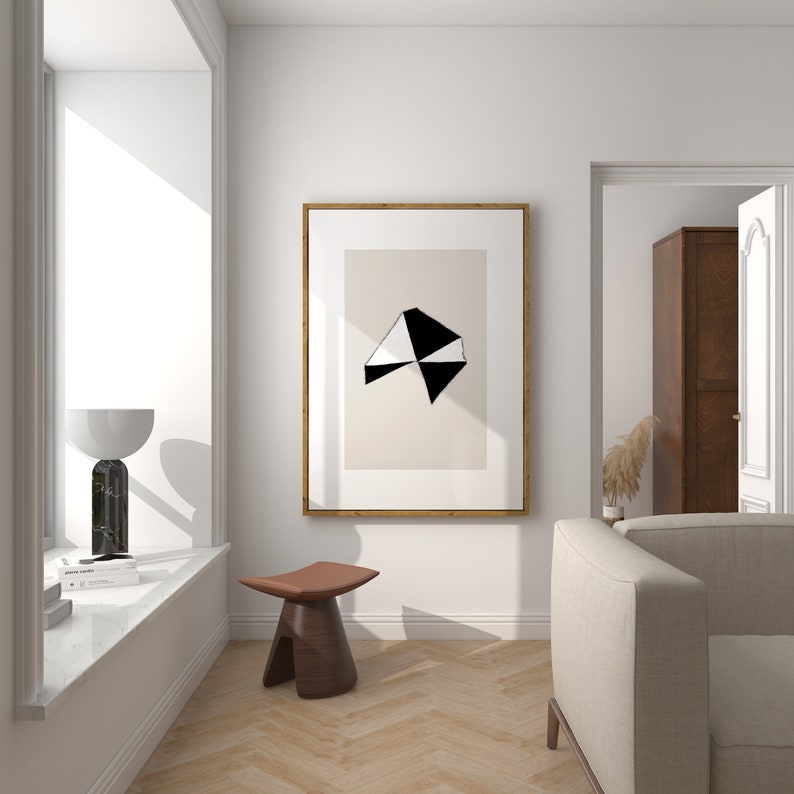 May include: A white and black geometric abstract art print in a wooden frame hangs on a white wall above a brown wooden stool. A white couch is in the background.