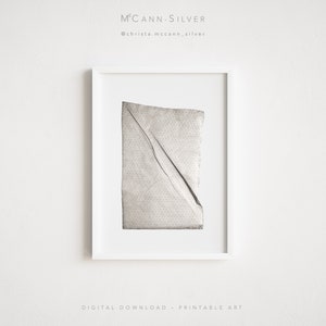 May include: A black and white photograph of a piece of crumpled paper with a dotted pattern. The paper is framed in a white frame. The image is titled "McCann-Silver" and includes the social media handle "@christa.mccann_silver".