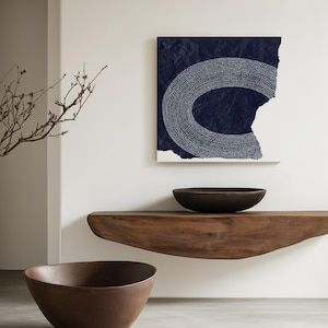 May include: Two brown wooden bowls, one on a wooden shelf and one on the floor, in front of a white wall with a blue and white abstract art print hanging on it.