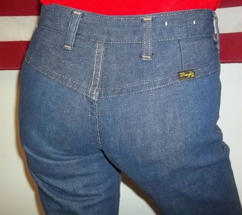 Peut inclure: Gros plan sur un jean en denim bleu avec une taille haute et une &eacute;tiquette Wrangler sur la poche arri&egrave;re. Le jean a une conception classique &agrave; cinq poches avec des coutures blanches et des passants de ceinture. Le tissu semble &ecirc;tre un denim de d&eacute;lavage moyen.