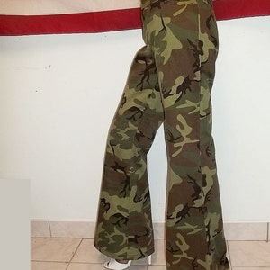 May include: Flared trousers in a camouflage pattern of green, brown, and black. The high-waisted trousers feature a wide leg design. The fabric appears durable, suitable for casual wear. The trousers are approximately 100 cm in length.