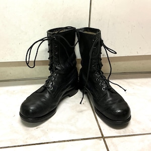 May include: A pair of black leather combat boots featuring a mid-calf height, rounded toes, and a lace-up front closure with black laces threaded through metal eyelets. The boots have a smooth finish, a structured heel, and a thick, durable sole.