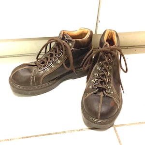 May include: A pair of brown leather boots with a lace-up design. The boots have a rugged, outdoor style with metal eyelets and a thick sole. The interior lining is a lighter brown color.