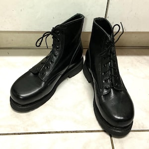 May include: A pair of black leather ankle boots featuring a rounded toe, a lace-up front with black eyelets, and thick black rubber soles. The boots have a smooth finish and black laces tied at the top, providing a sturdy and functional design.
