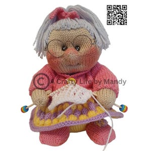 May include: A knitted doll depicting a grandmother wearing glasses, a pink sweater, and a patterned skirt. The doll is holding knitting needles and a piece of white knitted fabric. The doll has gray hair and a pink bow. The text "Crafty Life by Mandy" is visible.