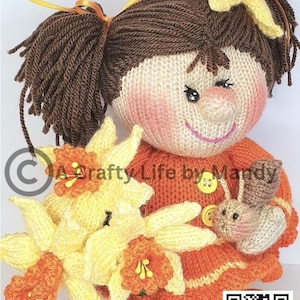 May include: A knitted doll with brown hair in pigtails wearing an orange and white striped dress. The doll is holding a bouquet of yellow and orange daffodils and a small brown knitted animal.