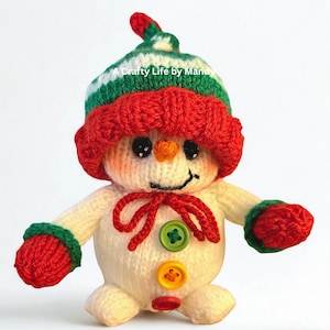 Könnte beinhalten: Ein handgestrickter Schneemann mit roter Mütze und Fäustlingen, grün-weiß gestreifter Mütze und roter Schleife. Der Schneemann hat schwarze Knopfaugen, eine orangefarbene Karottennase und ein gesticktes Lächeln. Er hat drei bunte Knöpfe auf der Vorderseite.