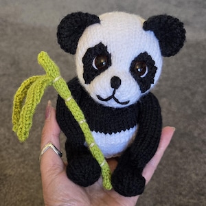 May include: A small, handcrafted crochet panda bear toy made with black and white yarn. The panda features large, dark brown plastic eyes, a black stitched nose and mouth, and is holding a textured, light green crocheted bamboo stalk.