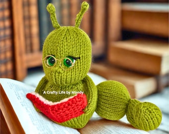 Puede incluir: Una figura de oruga verde tejida, con gafas doradas y leyendo un libro rojo. La figura tiene grandes ojos verdes y antenas. El texto "A Crafty Life by Mandy" es visible.
