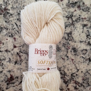 Może przedstawiać: Motka kremowej przędzy z etykietą "Briggs & Little Sofspun 2 Ply 100% Pure Wool 4 oz. 113g. Produkt Kanady."