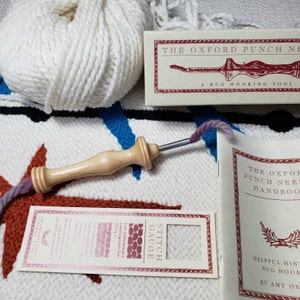 Könnte beinhalten: Nahaufnahme eines Teppich-Häkel-Sets mit einer hölzernen Stichnadel, einer Spule weißen Garns, einer Stichlehre und einem Heft mit dem Titel "The Oxford Punch Needle Handbook".