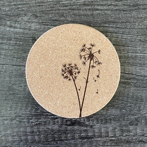 May include: A round cork coaster with a laser-etched design of two dandelions. The dandelions are black and the background is a light brown.