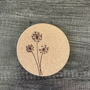 May include: A round cork coaster with a laser-etched design of three dandelion flowers.