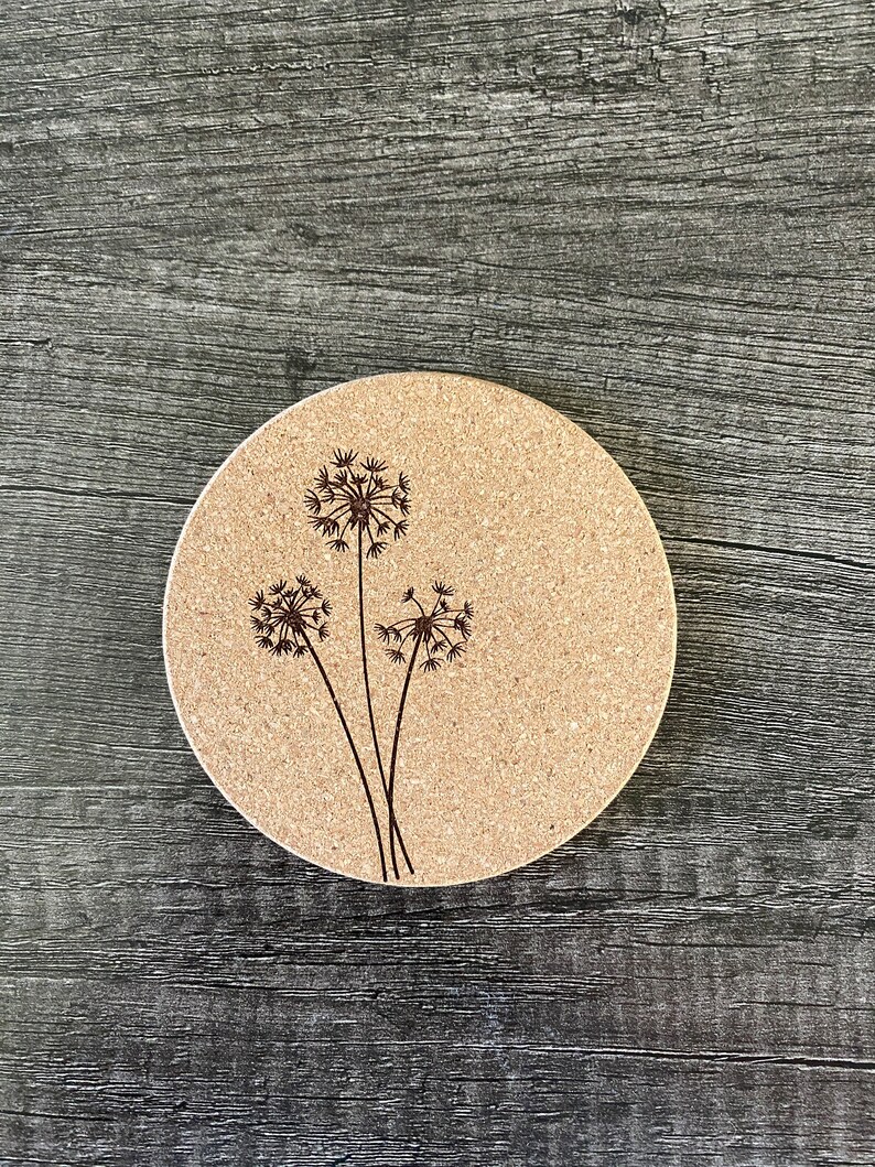 May include: A round cork coaster with a laser-etched design of three dandelion flowers.
