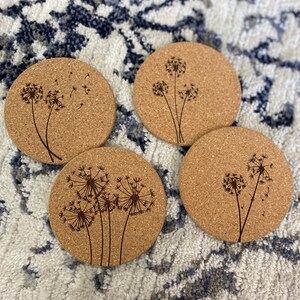 May include: Four round cork coasters with a laser-etched design of dandelions with seeds blowing in the wind.