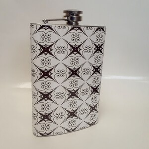 May include: A silver flask with a black and white geometric pattern. The flask has a screw-on cap.