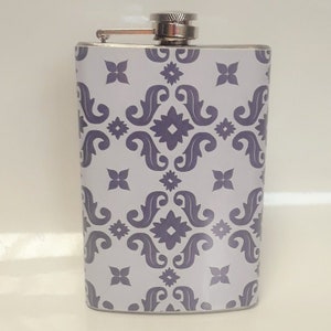 May include: A silver flask with a purple and white geometric pattern. The flask has a screw-on cap.