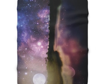 Puede incluir: Una manta rectangular con un diseño celestial. La manta está dividida verticalmente, con una galaxia púrpura y azul estrellada a la izquierda y una galaxia más oscura a la derecha. Una luna llena es visible en la parte inferior.