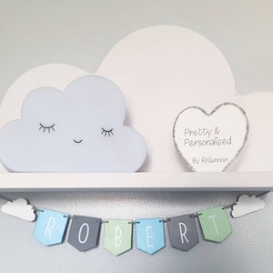May include: A white wooden shelf with a cloud-shaped nightlight and a heart-shaped sign that reads "Pretty & Personalised By Rhiannon". A banner with the name "ROBERT" hangs below the shelf.