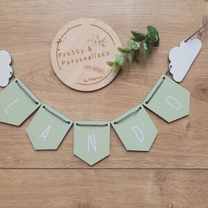 May include: A green and white wooden banner with the word "LANDO" spelled out in white letters. The banner is strung with gray string and has white cloud shapes on either end.