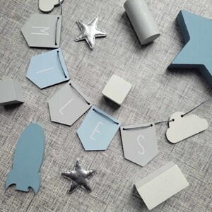 May include: A blue and gray baby mobile with a rocket, stars, clouds, and a banner that reads "MILES".