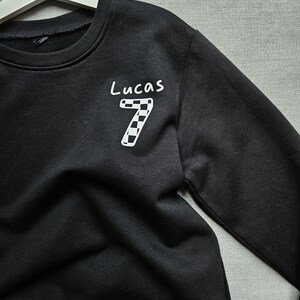 May include: Black sweatshirt with a white chequered number 7 and the name Lucas written above it.