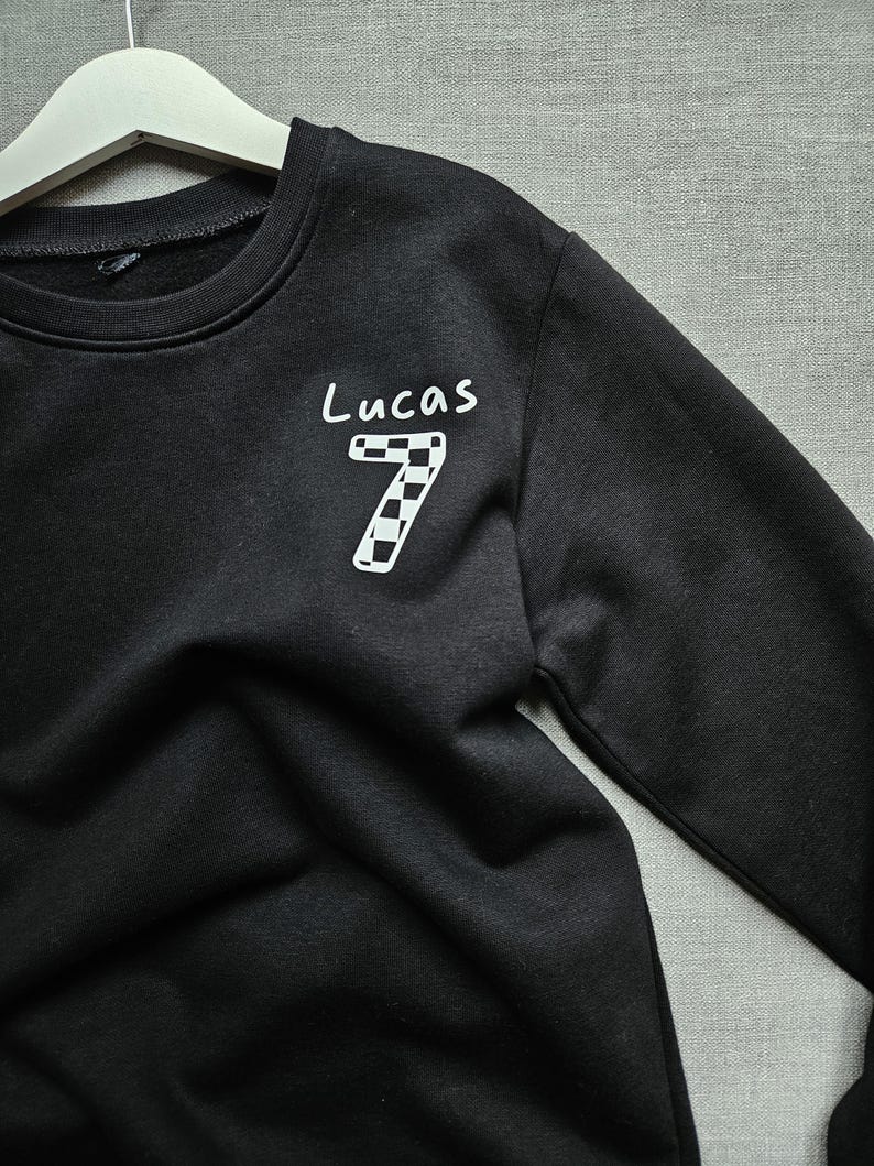May include: Black sweatshirt with a white chequered number 7 and the name Lucas written above it.