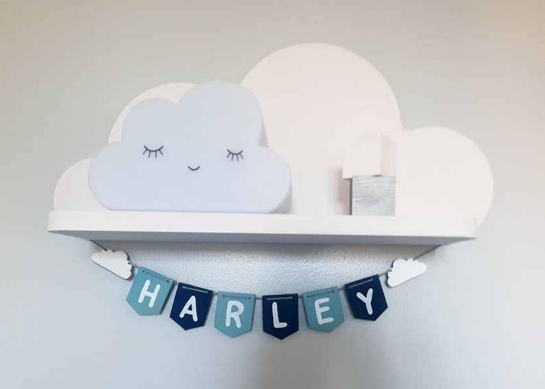 May include: A white shelf with a cloud-shaped nightlight and a wooden block. Below the shelf is a blue and white banner with the name "HARLEY" spelled out.