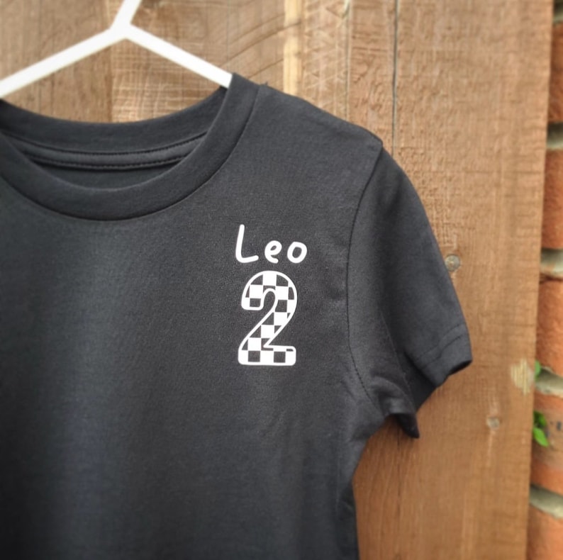 May include: Black t-shirt with a white checkered number "2" and the name "Leo" written in white.
