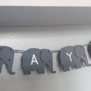 K&ouml;nnte beinhalten: Ein grauer Elefantenbanner mit dem Namen "Faye" in wei&szlig;en Buchstaben.