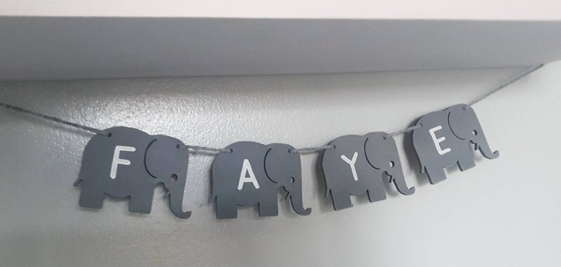 K&ouml;nnte beinhalten: Ein grauer Elefantenbanner mit dem Namen "Faye" in wei&szlig;en Buchstaben.