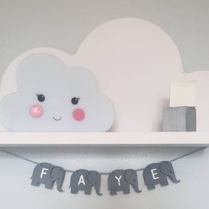 K&ouml;nnte beinhalten: Ein wei&szlig;es, wolkenf&ouml;rmiges Regal mit einer leuchtenden Wolke und einem grauen Elefantenbanner mit der Aufschrift "FAYE".
