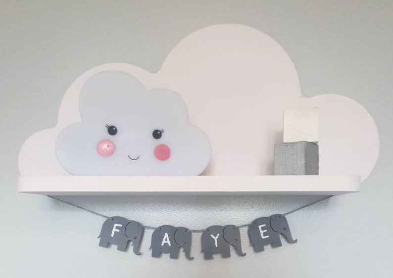 K&ouml;nnte beinhalten: Ein wei&szlig;es, wolkenf&ouml;rmiges Regal mit einer leuchtenden Wolke und einem grauen Elefantenbanner mit der Aufschrift "FAYE".