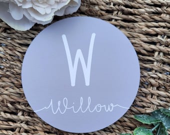 Könnte beinhalten: Ein rundes, hellgraues Holzschild mit einem weißen Buchstaben W und dem Wort "Willow" darunter in Kursivschrift.