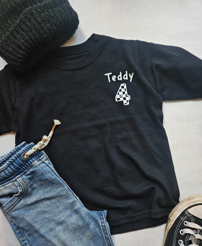 May include: Black long-sleeved t-shirt with the name "Teddy" and a chequered number "4" printed on the front.