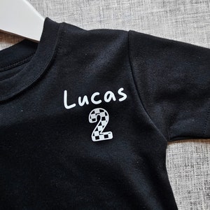 May include: Black t-shirt with white text that says "Lucas" and a chequered number "2" on the front.