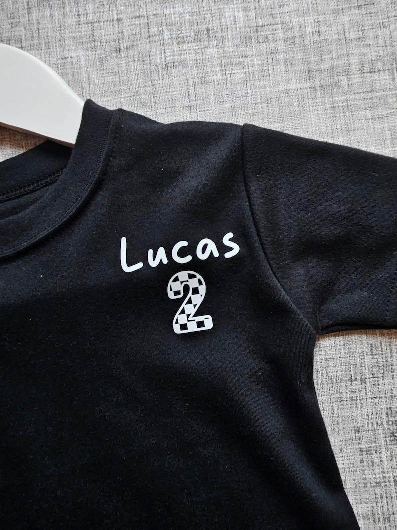 May include: Black t-shirt with white text that says "Lucas" and a chequered number "2" on the front.