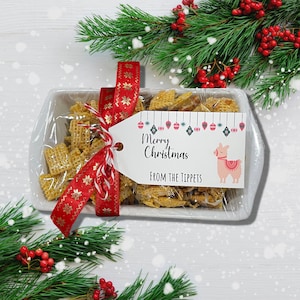 K&ouml;nnte beinhalten: Eine wei&szlig;e Keramik-Schale gef&uuml;llt mit einem Snack-Mix, gebunden mit einem roten und goldenen Band und einem Geschenkanh&auml;nger mit der Aufschrift "Frohe Weihnachten von den Tippets". Die Schale ist von einem gr&uuml;nen Tannenzweig mit roten Beeren umgeben.