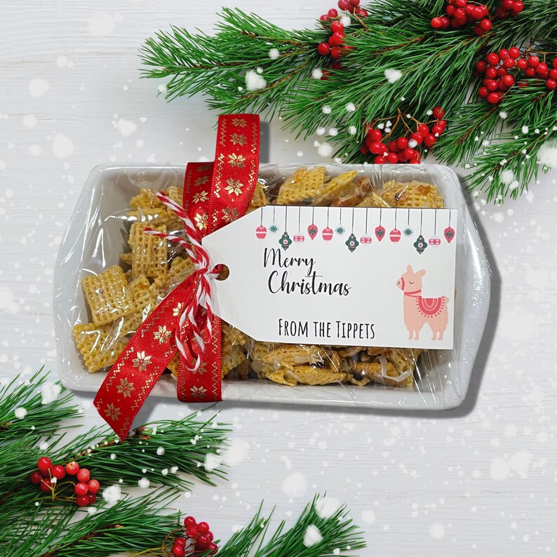 K&ouml;nnte beinhalten: Eine wei&szlig;e Keramik-Schale gef&uuml;llt mit einem Snack-Mix, gebunden mit einem roten und goldenen Band und einem Geschenkanh&auml;nger mit der Aufschrift "Frohe Weihnachten von den Tippets". Die Schale ist von einem gr&uuml;nen Tannenzweig mit roten Beeren umgeben.