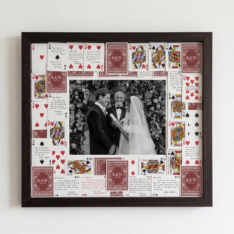May include: A framed wedding photo surrounded by playing cards. The frame is dark brown, and the photo is in black and white. The playing cards are red and white, with some featuring the initials "K&W".