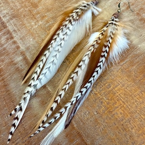 May include: A pair of long, brown and white feather earrings with a wooden bead accent. The feathers are layered and have a chevron pattern.