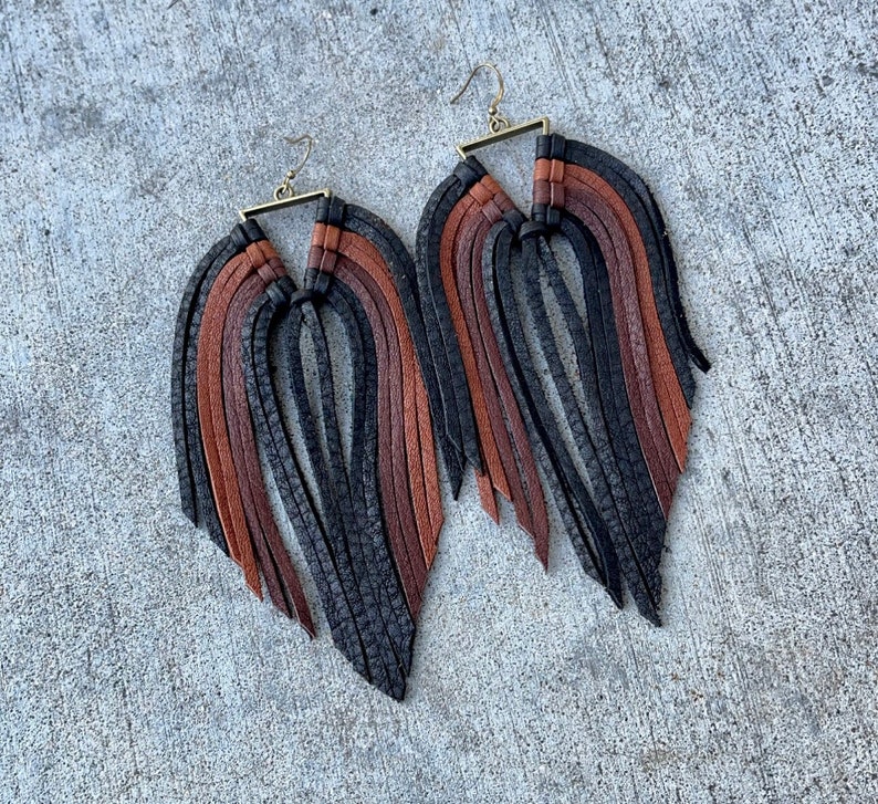 May include: A pair of long, black and brown leather fringe earrings with a gold-toned metal triangle at the top.