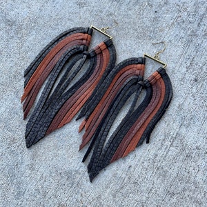 May include: A pair of long, black, brown, and rust colored leather fringe earrings with a square brass hook.