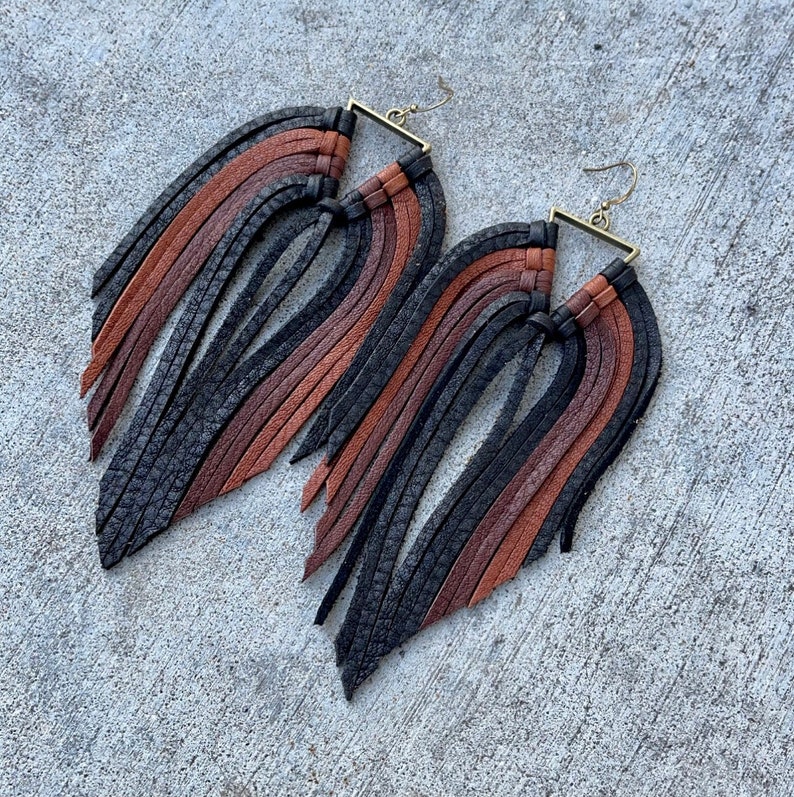 May include: A pair of long, black, brown, and rust colored leather fringe earrings with a square brass hook.