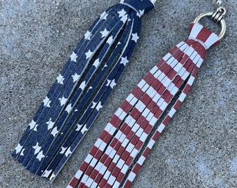May include: A pair of dangle earrings with a tassel design. One earring features a blue and white American flag pattern, while the other earring features a red and white striped pattern.