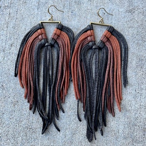 May include: A pair of long, black and brown leather fringe earrings with a triangular metal frame.